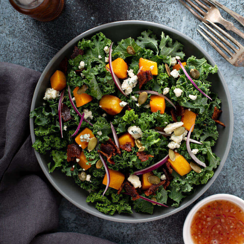 Luxurious kale salad in a bowl on table with a side of dressing
