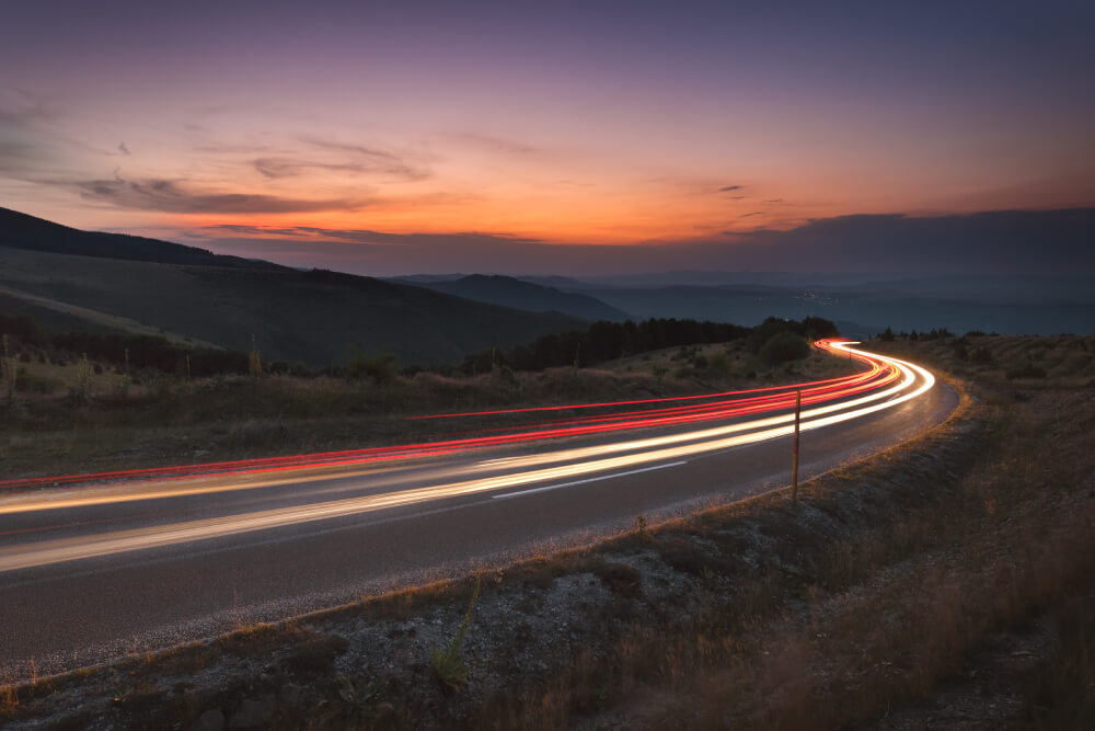 Driving on winding road at dusk down the mountain. Light trails at beautiful sunset, long exposure image.