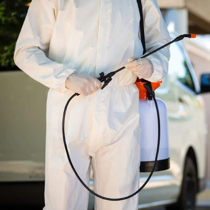 Exterminator in a white jumpsuit with a spray can for pest control